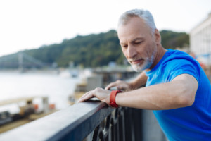 Older man looks at his fitness watch while standing outside.