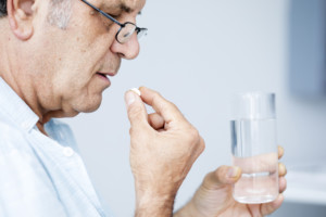 A senior man takes a supplement while holding a glass of water